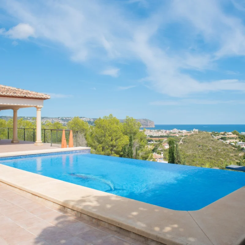 Piscine à débordement avec terrasse en grès et porche à colonnes classiques. Offre une vue panoramique sur la mer Méditerranée et la côte de Jávea.