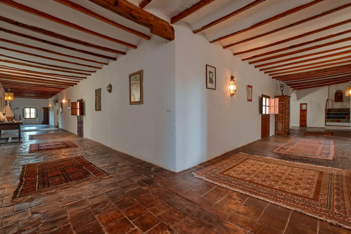 Amplio pasillo con vigas de madera vista, suelos de terracota original y alfombras tradicionales que decoran el espacio de paso.