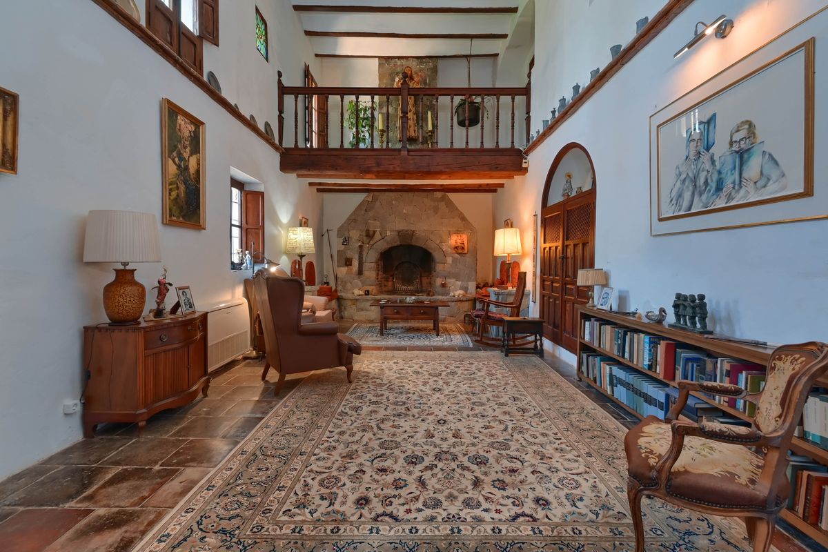 Amplio salón con chimenea de piedra natural, vigas de madera vista y una galería superior de madera sobre suelos de baldosa rústica tradicional.