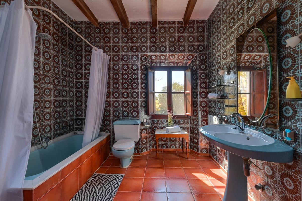 Baño de estilo rústico con azulejos geométricos, sanitarios en azul pastel, vigas de madera originales y suelos de terracota natural.