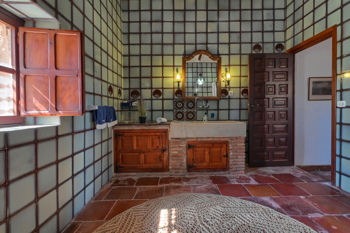 Baño tradicional con lavabo de piedra sobre base de ladrillo, armarios de madera rústica, suelo de terracota y paredes revestidas con azulejos de rejilla.