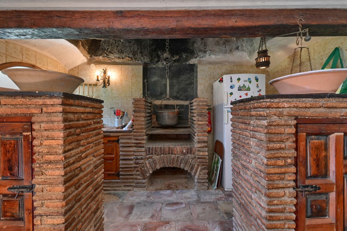 Cocina histórica con hogar tradicional de ladrillo visto, viga de madera original y una olla de hierro suspendida sobre el fuego.