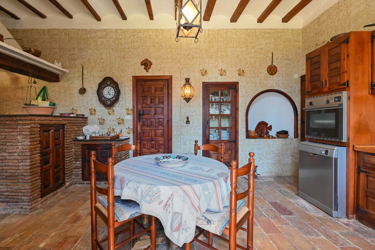 Cocina rústica tradicional con vigas de madera vistas, suelo de barro cocido y chimenea de obra. Paredes decoradas con azulejos y electrodomésticos integrados.