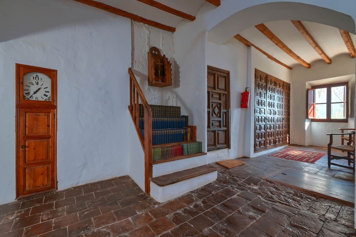 Distribuidor con suelos de barro, vigas de madera y reloj de pared encastrado. Incluye una pequeña escalera con librería integrada y carpintería tradicional de madera.