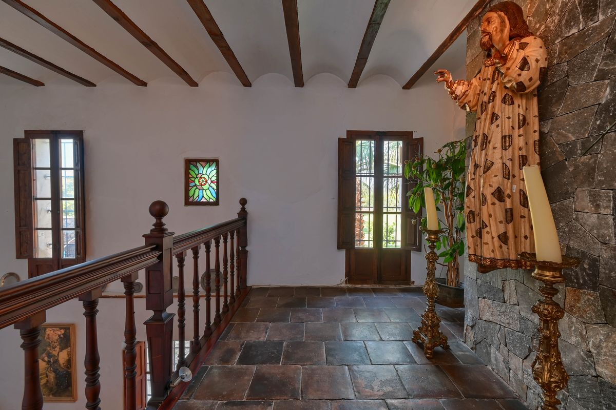 Distribuidor superior con suelos de barro cocido, vigas de madera vista, barandilla torneada y una pared de piedra natural decorada con imaginería religiosa.