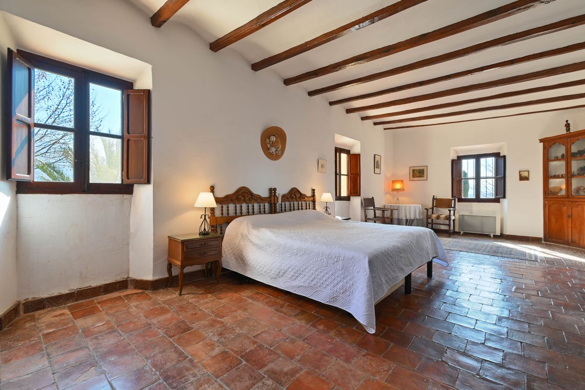 Dormitorio rústico con vigas de madera a la vista, suelos de terracota auténtica y mobiliario de madera tallada de estilo tradicional.