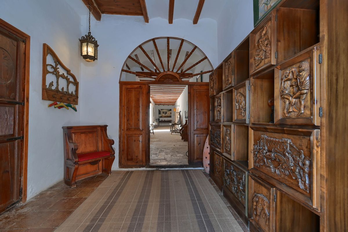 Hall de entrada con armarios de madera tallada, vigas vistas y un gran portón de arco con ventanal superior que da paso al pasillo principal.