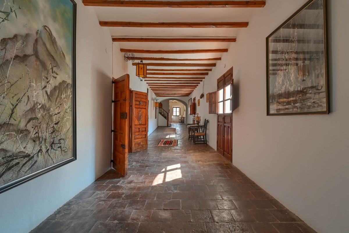 Pasillo con suelos de barro cocido, vigas de madera vista y puertas artesanales de madera tallada que reflejan el carácter histórico de la finca.