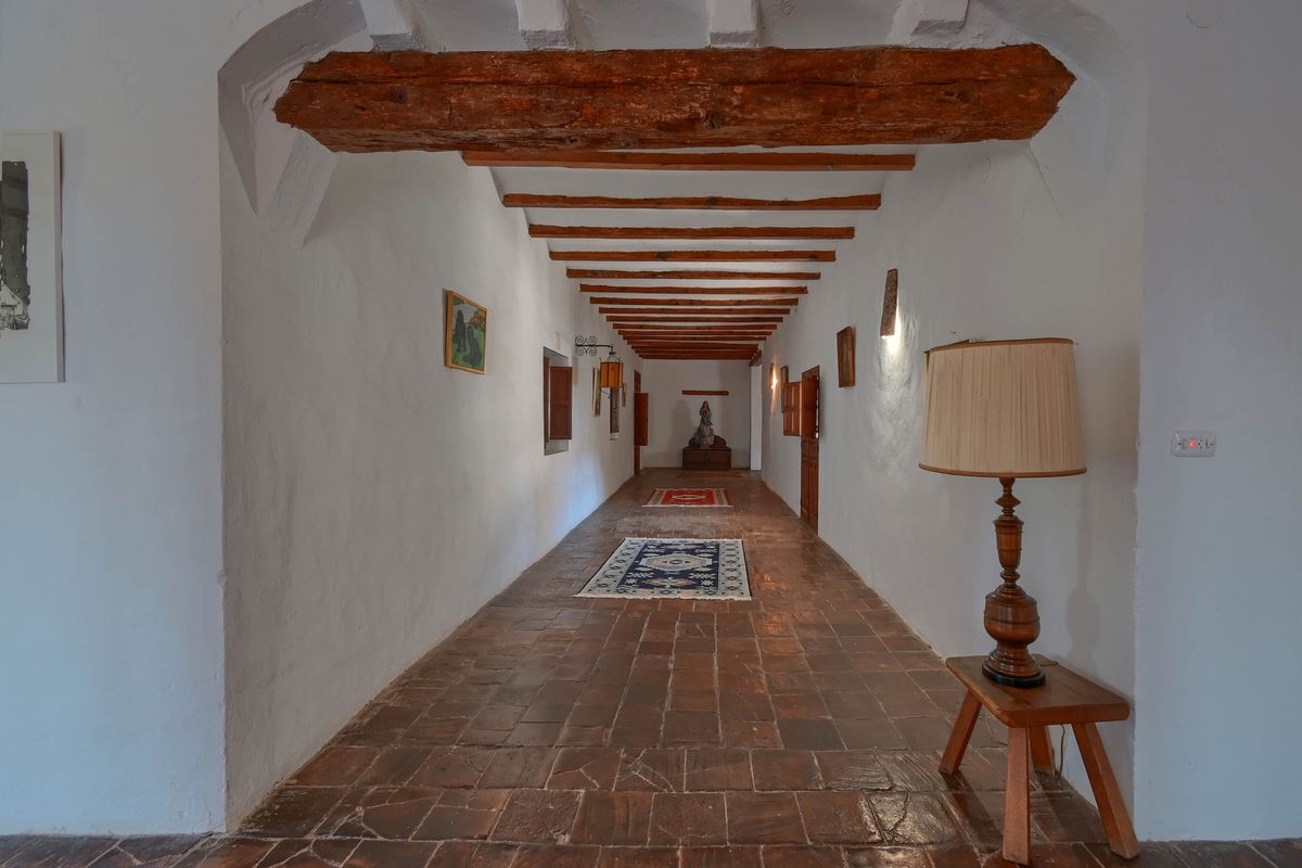 Pasillo de estilo tradicional con suelos de baldosas de barro, paredes encaladas y un techo caracterizado por vigas de madera rústica expuestas.