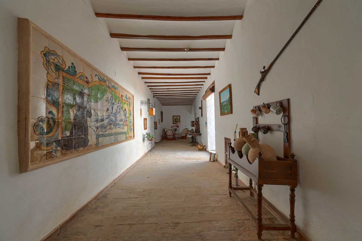 Pasillo histórico con vigas de madera expuestas, suelo de piedra natural y un gran mural de azulejos cerámicos pintados a mano.
