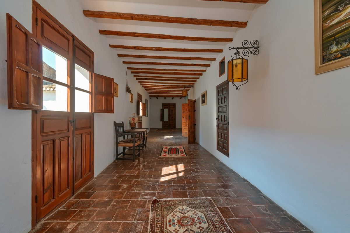 Pasillo señorial con vigas de madera vistas, suelos de barro cocido y puertas de madera maciza con contraventanas tradicionales.