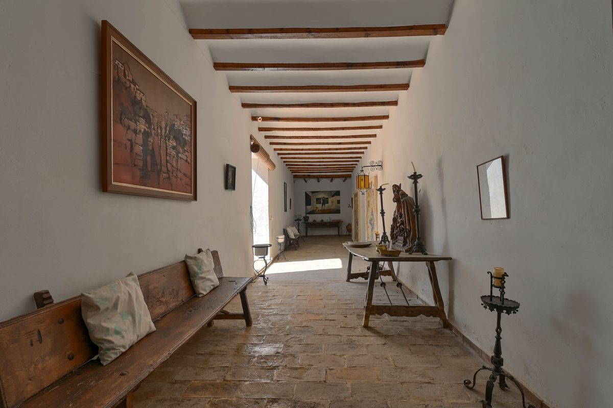Pasillo señorial con vigas de madera vistas, suelos de barro original y mobiliario de época que resalta el carácter histórico de la finca.
