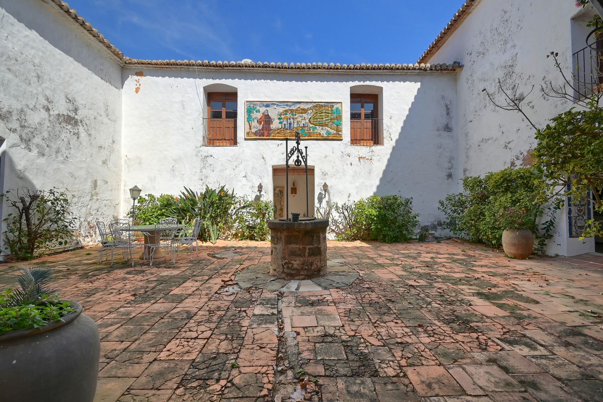 Patio interior tradicional con suelo de barro cocido, pozo central de piedra y un gran mural cerámico decorativo sobre la fachada blanca.