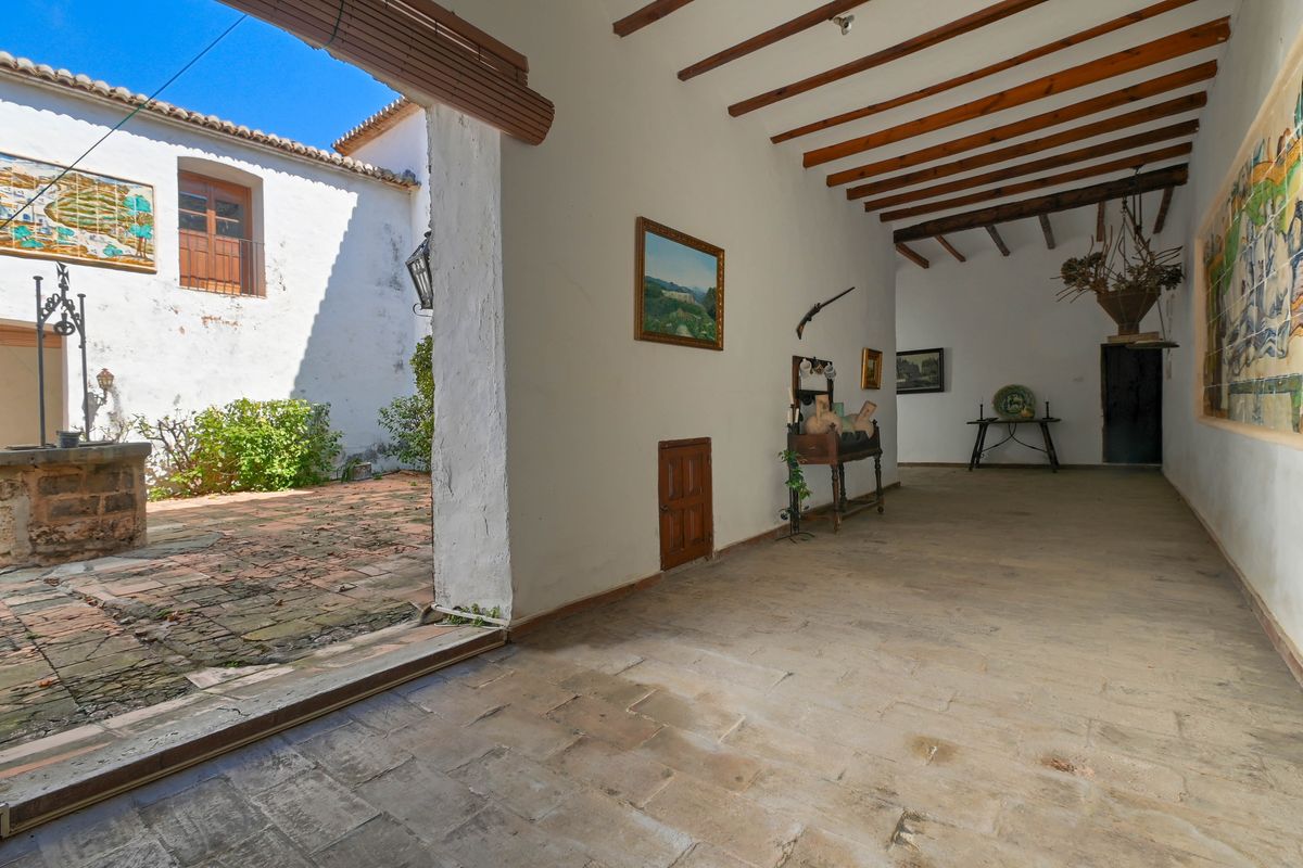 Porche cubierto con vigas de madera expuestas y suelo de piedra, que incluye un mural cerámico tradicional y vistas a un patio interior con un pozo antiguo.