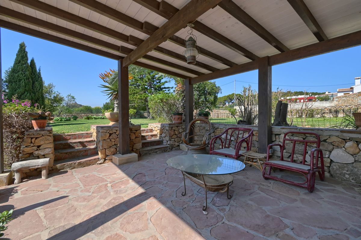 Porche cubierto con vigas de madera vista, suelo de piedra natural y muros de mampostería tradicional con acceso directo al jardín mediterráneo.