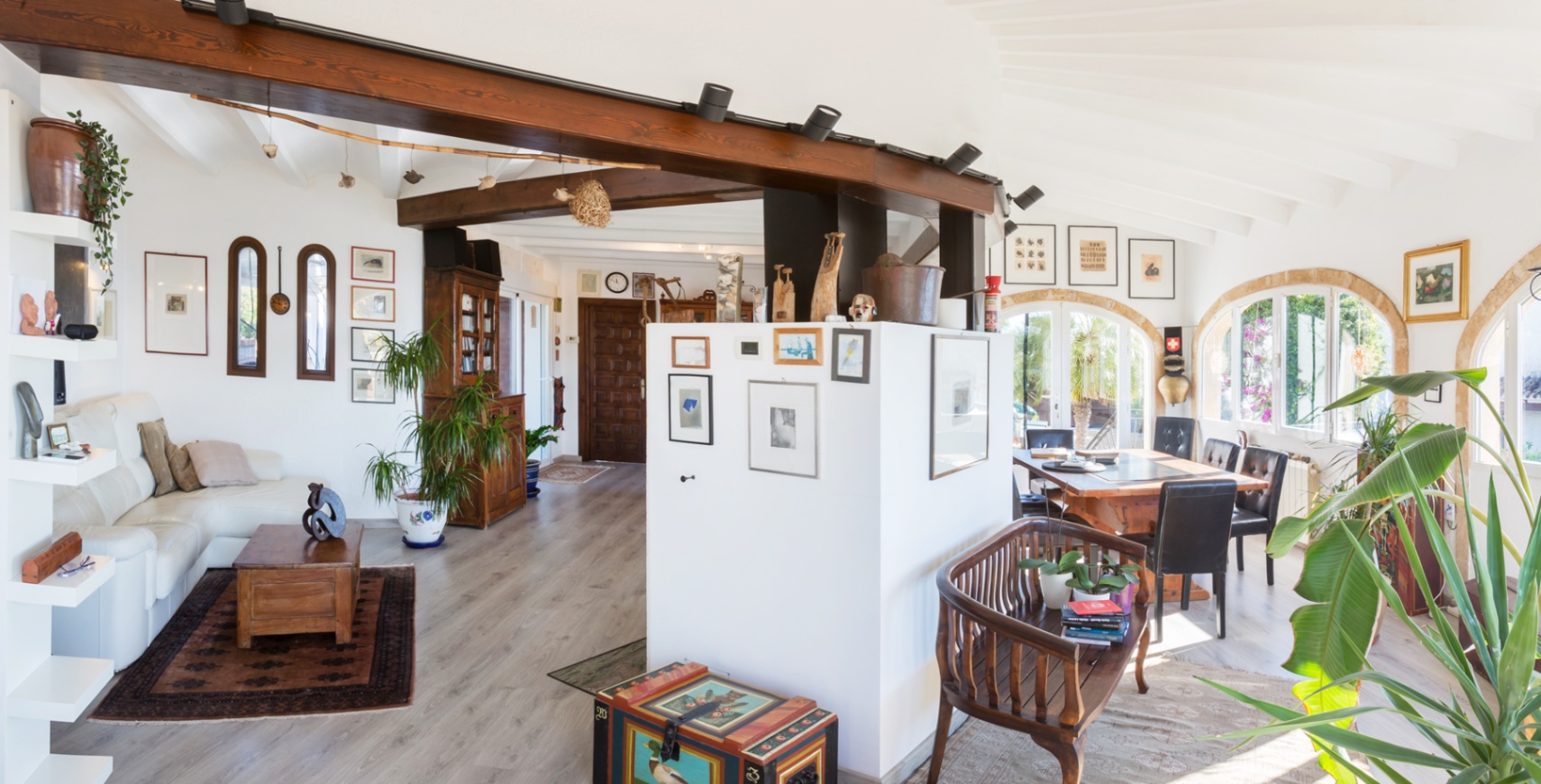 Espacio diáfano con vigas de madera vista, techos abovedados y ventanales de arco que iluminan el salón-comedor con luz natural y suelos de madera clara.