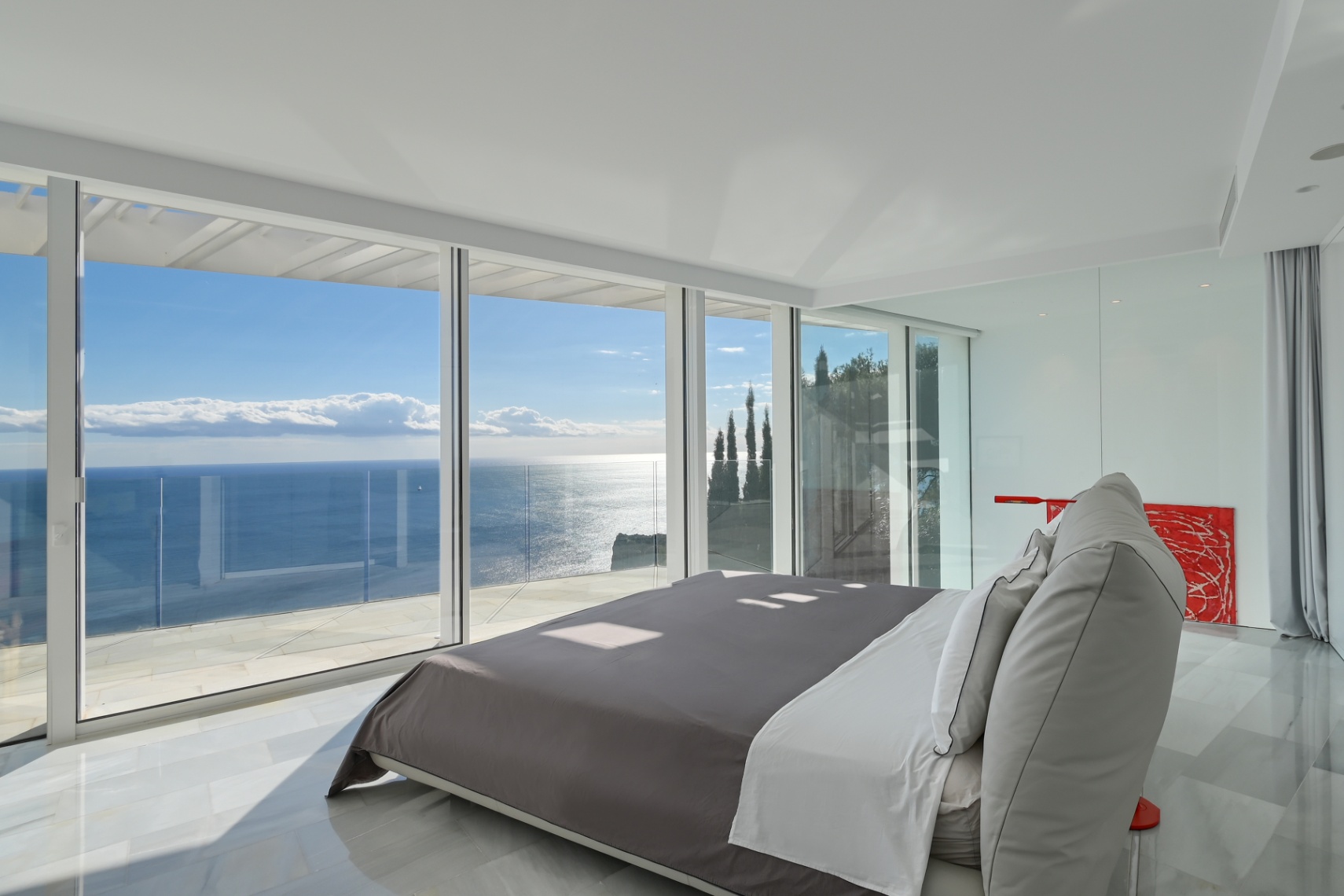 Dormitorio principal moderno con ventanales de suelo a techo, suelo de mármol blanco y vistas panorámicas al mar Mediterráneo desde una terraza privada.