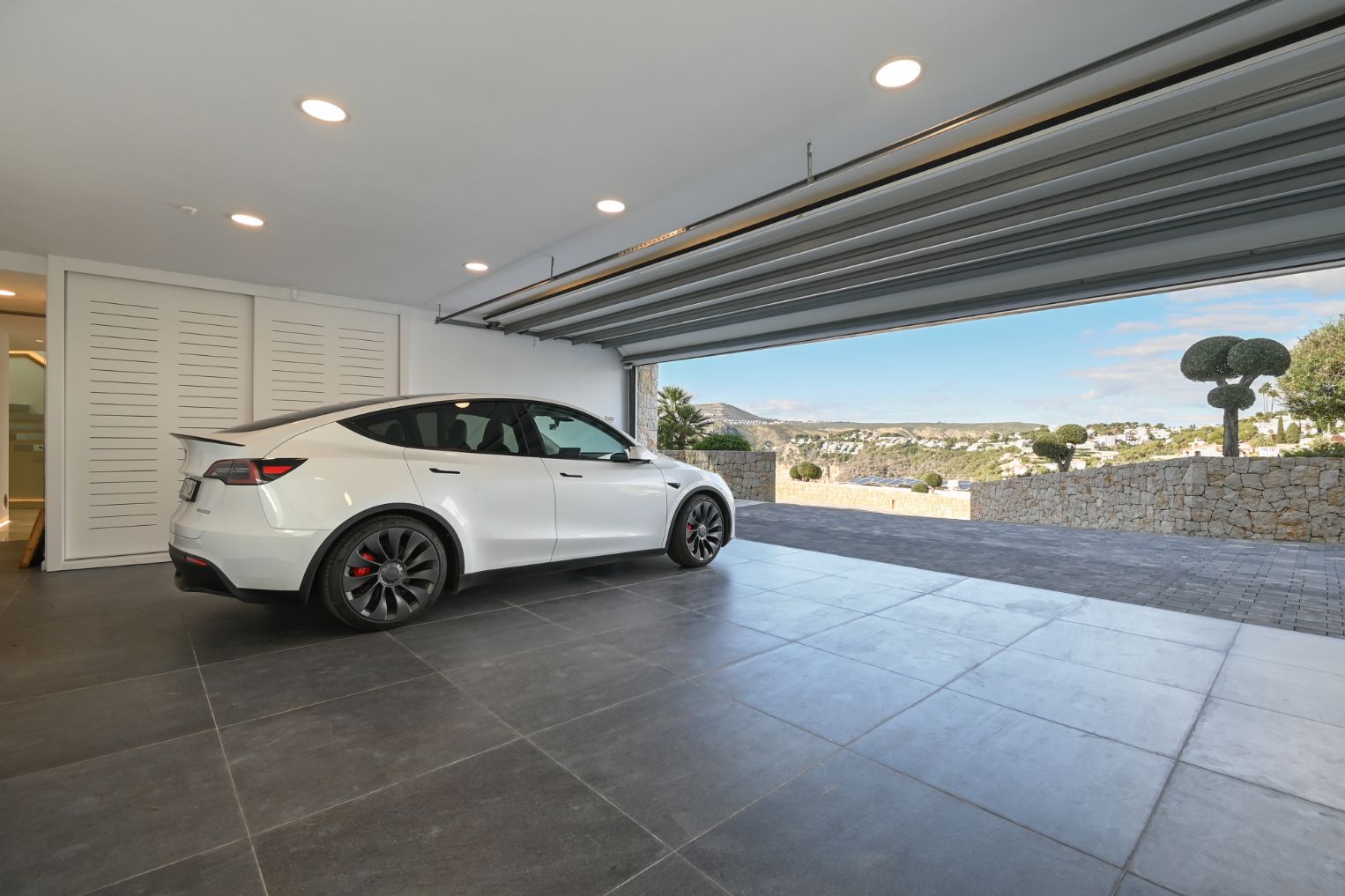 Garaje moderno con baldosas grises de gran formato, luces empotradas y vistas al valle desde la entrada pavimentada con piedra natural.