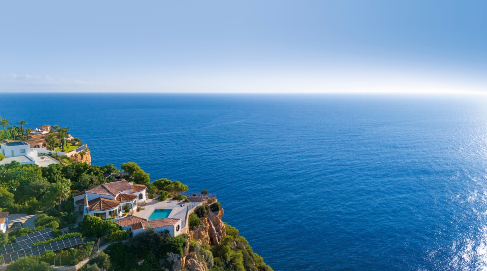 Vista aérea de una villa en el acantilado con tejados de terracota, terraza con piscina y vistas panorámicas al mar Mediterráneo.
