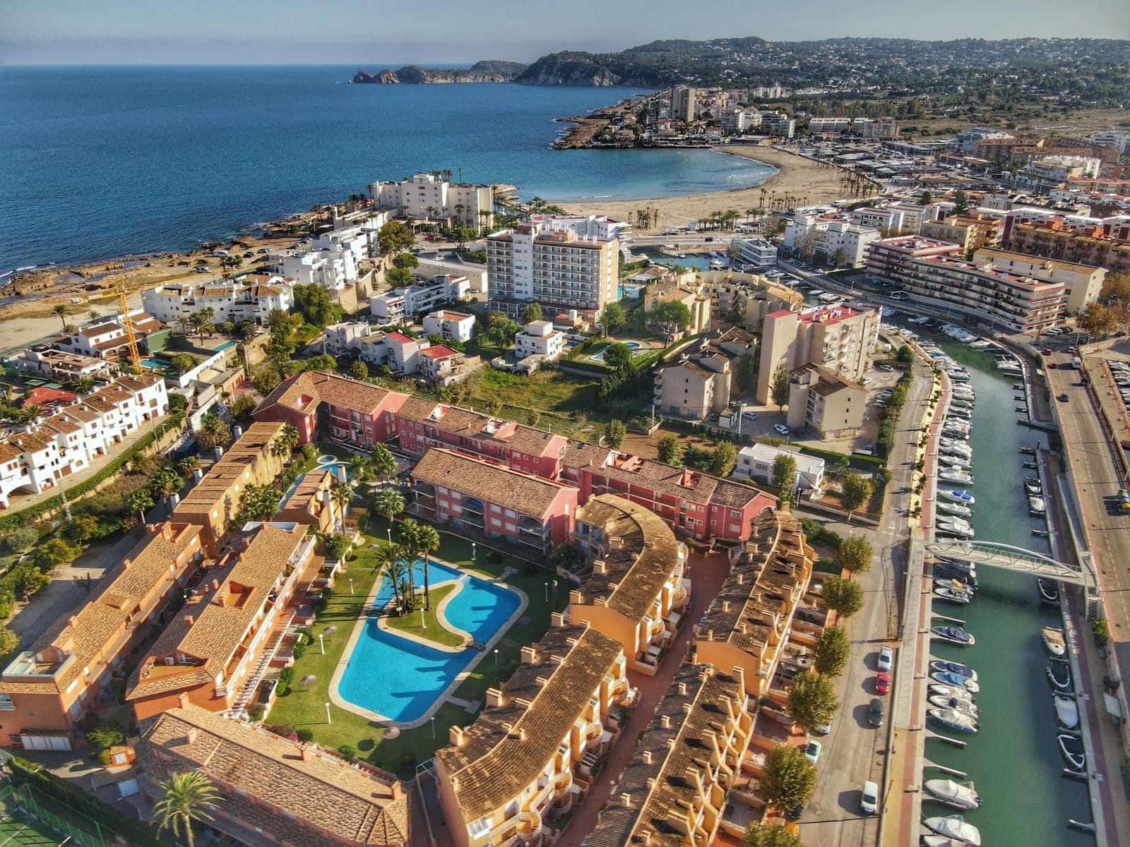 Vista aérea de un complejo residencial con piscina comunitaria, rodeado de canales náuticos y con vistas panorámicas hacia la costa mediterránea.