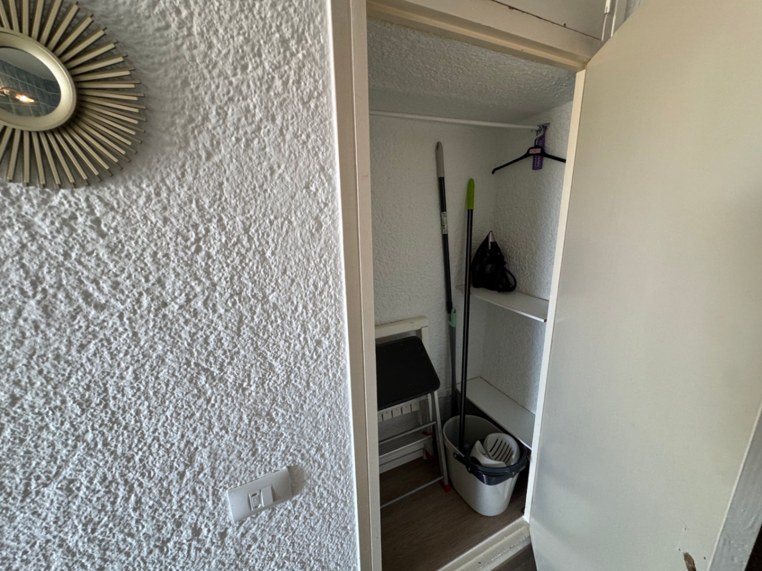 Armario de limpieza compacto con estanterías blancas, barra para colgar y espacio para utensilios domésticos.