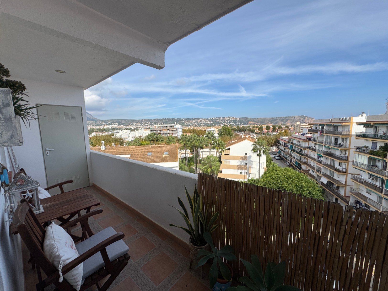 Balcón con suelo de terracota, mobiliario de madera y cerramiento de bambú. Ofrece vistas despejadas al entorno urbano y a las montañas circundantes.