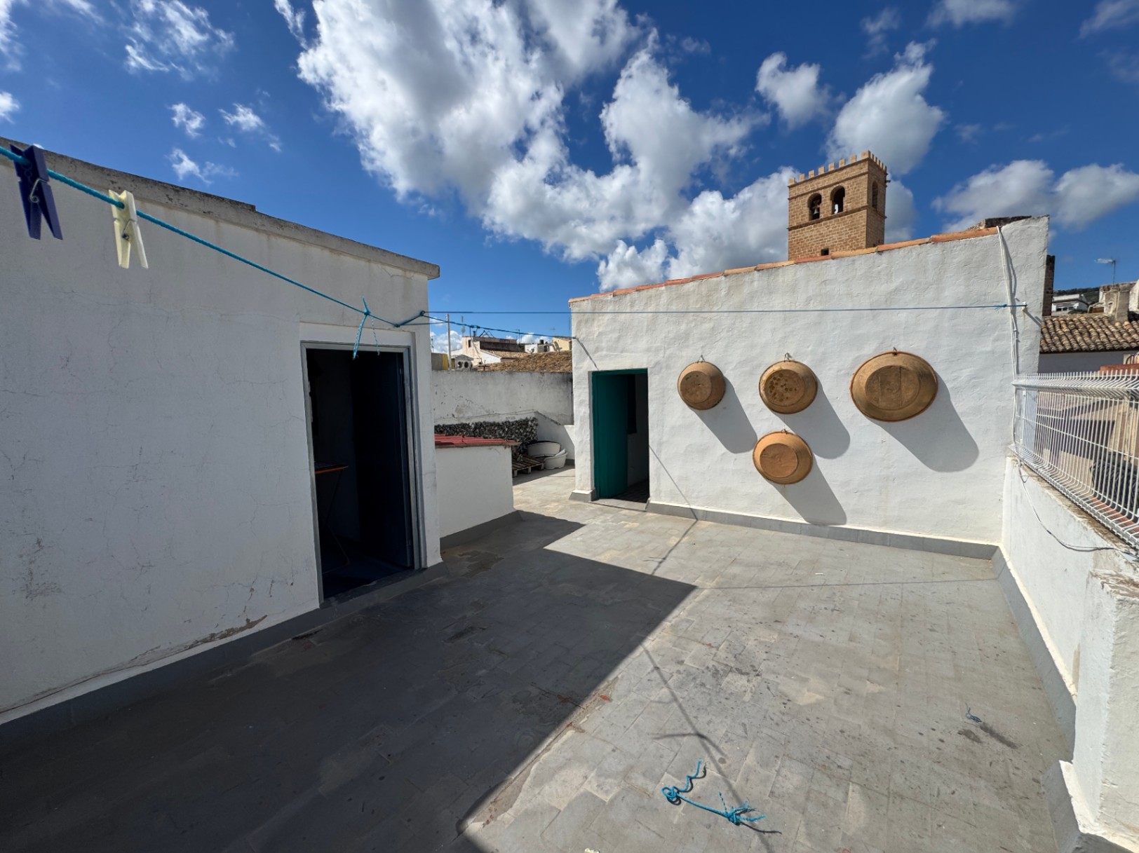 Azotea con suelo de baldosas de piedra, paredes encaladas decoradas con cuencos de barro y vistas a una torre histórica bajo un cielo despejado.