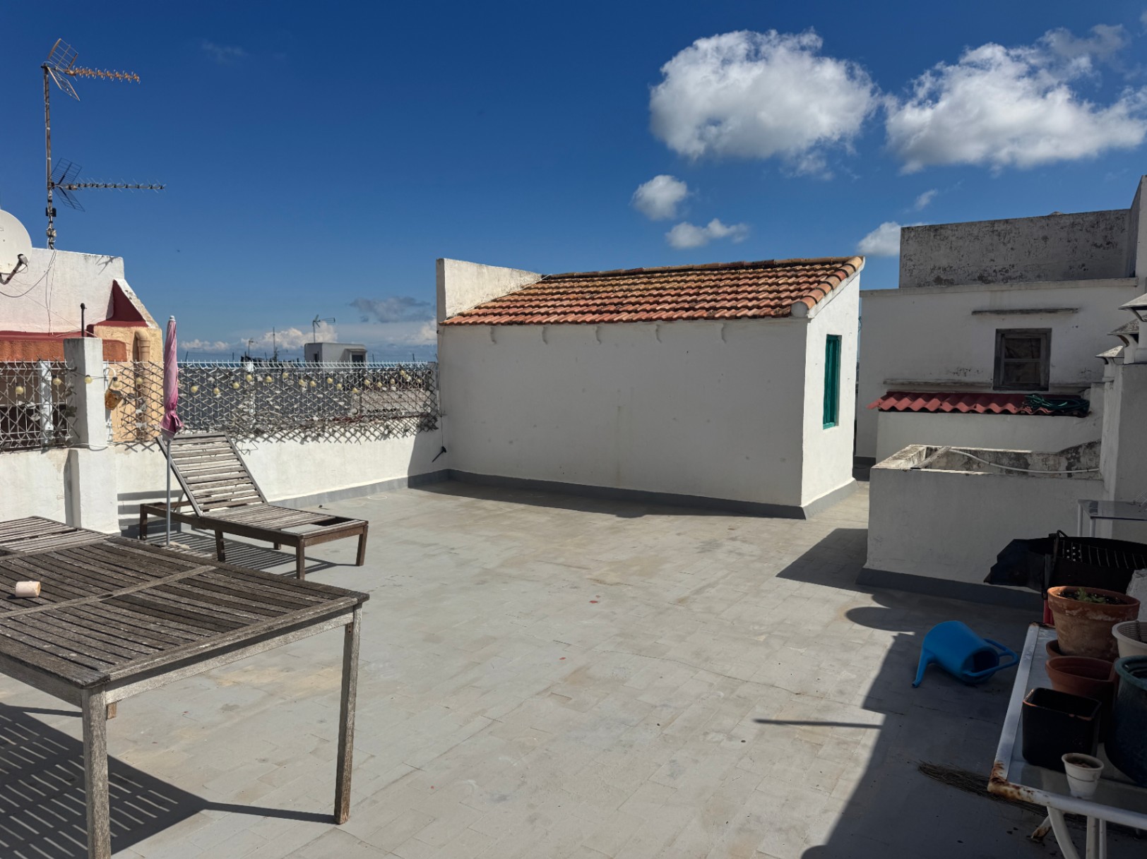 Terraza en la azotea con suelo cerámico, mobiliario de madera envejecida y una pequeña construcción blanca con tejado de teja árabe tradicional.