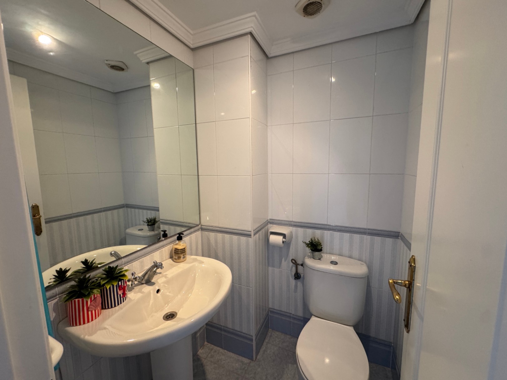 Baño funcional con lavabo de pedestal, inodoro blanco y paredes alicatadas con una cenefa decorativa en tonos azulados.