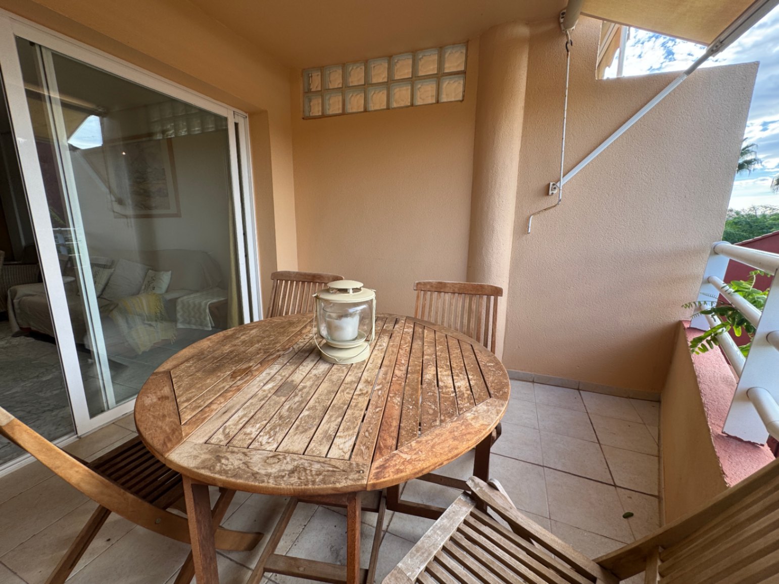 Terraza cubierta con conjunto de comedor de madera circular y suelos cerámicos, conectada al interior mediante amplios ventanales correderos.