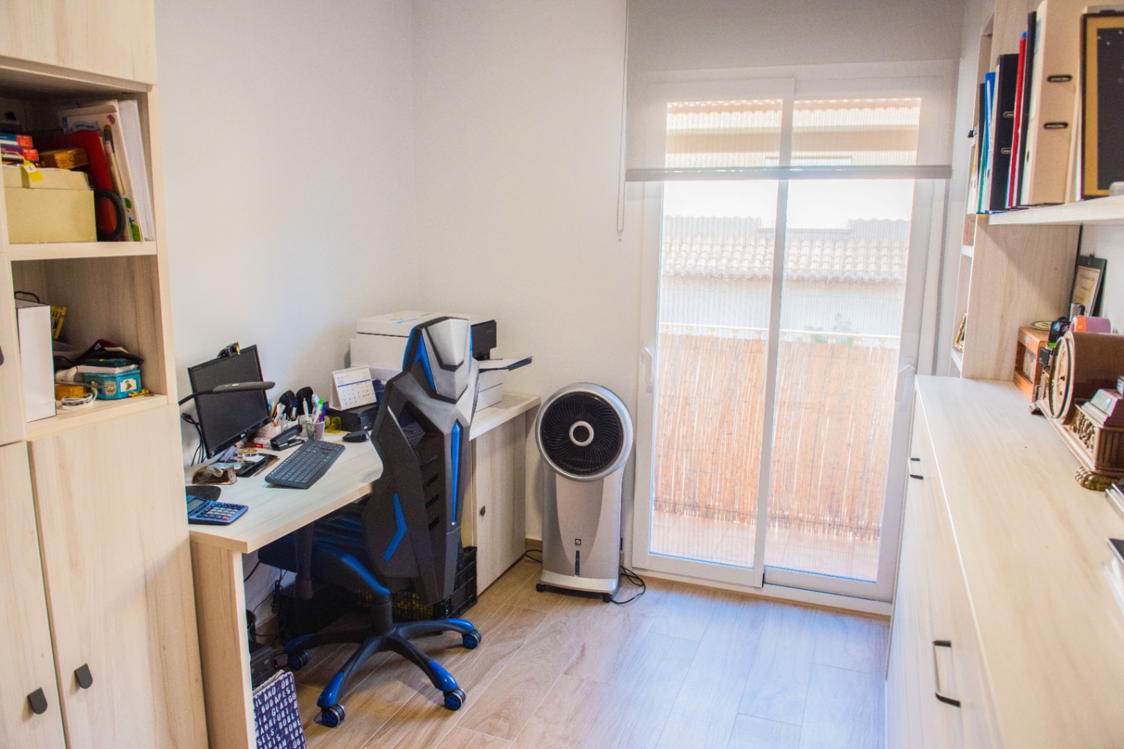 Despacho funcional con escritorio de madera clara, silla ergonómica y estanterías a medida. Dispone de acceso a un balcón privado a través de una puerta corredera.