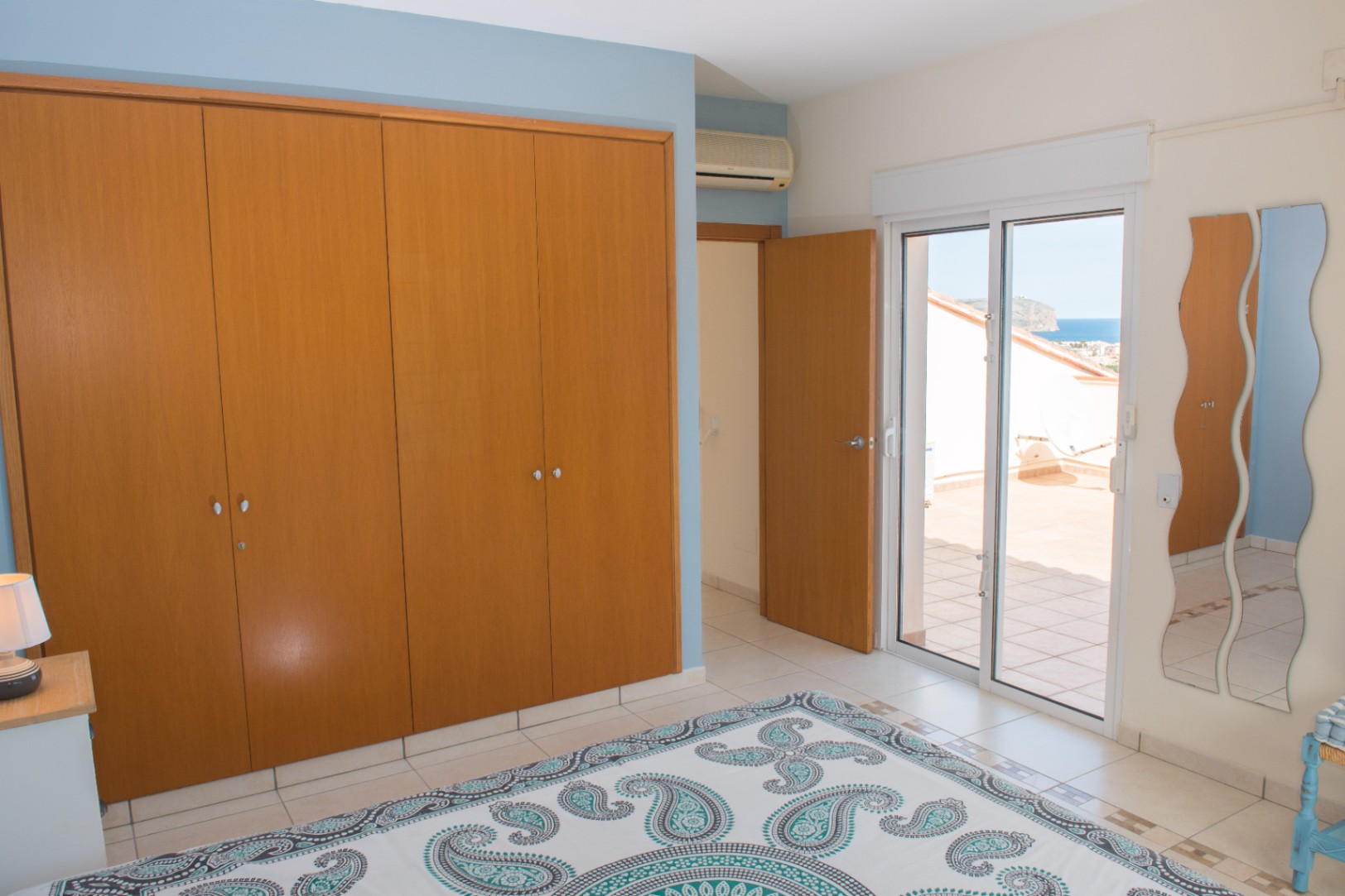 Dormitorio con amplio armario empotrado de madera, paredes en tonos azules y acceso directo a una terraza privada con vistas al mar Mediterráneo.