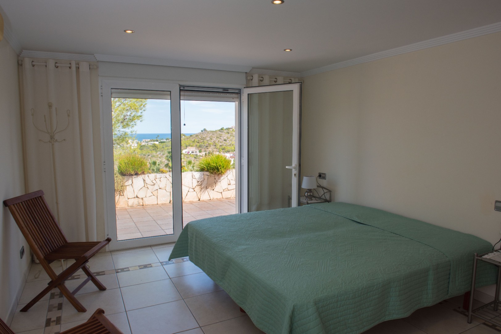 Dormitorio luminoso con acceso directo a una terraza privada, ofreciendo vistas despejadas al mar y a las colinas mediterráneas a través de grandes ventanales.