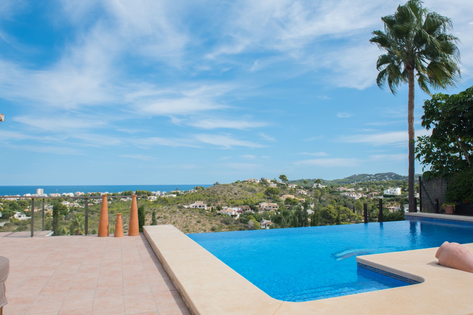 Piscina infinita con borde de piedra y vistas panorámicas al mar Mediterráneo. La terraza cuenta con suelos de terracota y elementos decorativos cerámicos.