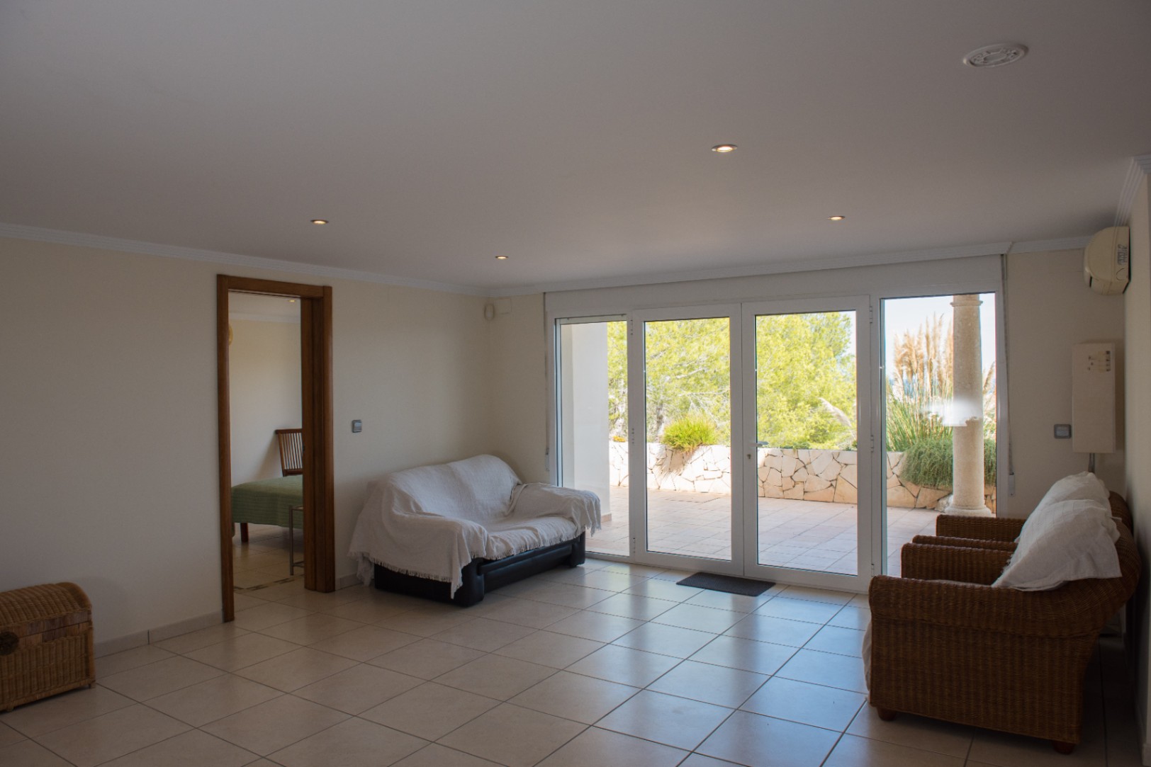 Salón con suelos cerámicos y amplios ventanales de acceso a la terraza. Incluye sillones de mimbre, iluminación empotrada y vistas al jardín exterior.