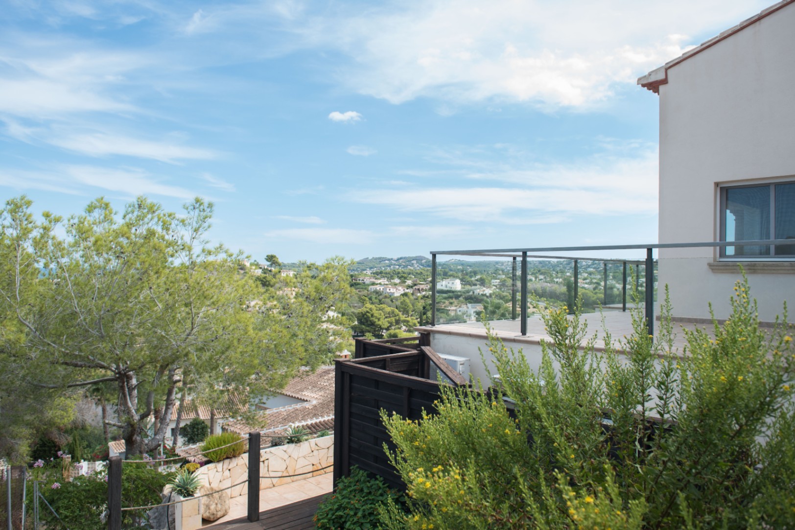 Terraza elevada con barandilla de cristal y metal que ofrece vistas panorámicas al valle y la vegetación mediterránea circundante.