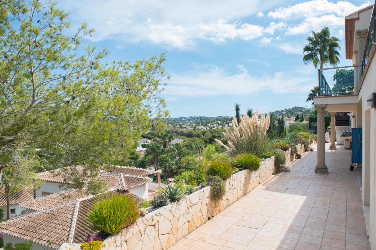 Terraza elevada con suelo cerámico y jardinera de piedra natural. Ofrece vistas despejadas al valle, tejados tradicionales y abundante vegetación mediterránea.