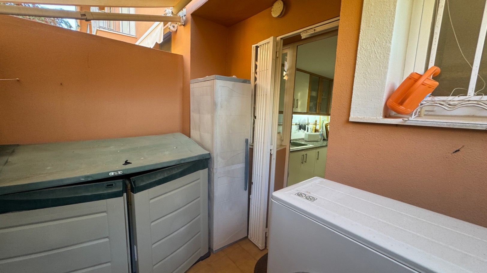 Patio de servicio con paredes color terracota, armarios de almacenaje exterior y acceso directo a la cocina mediante una puerta plegable.