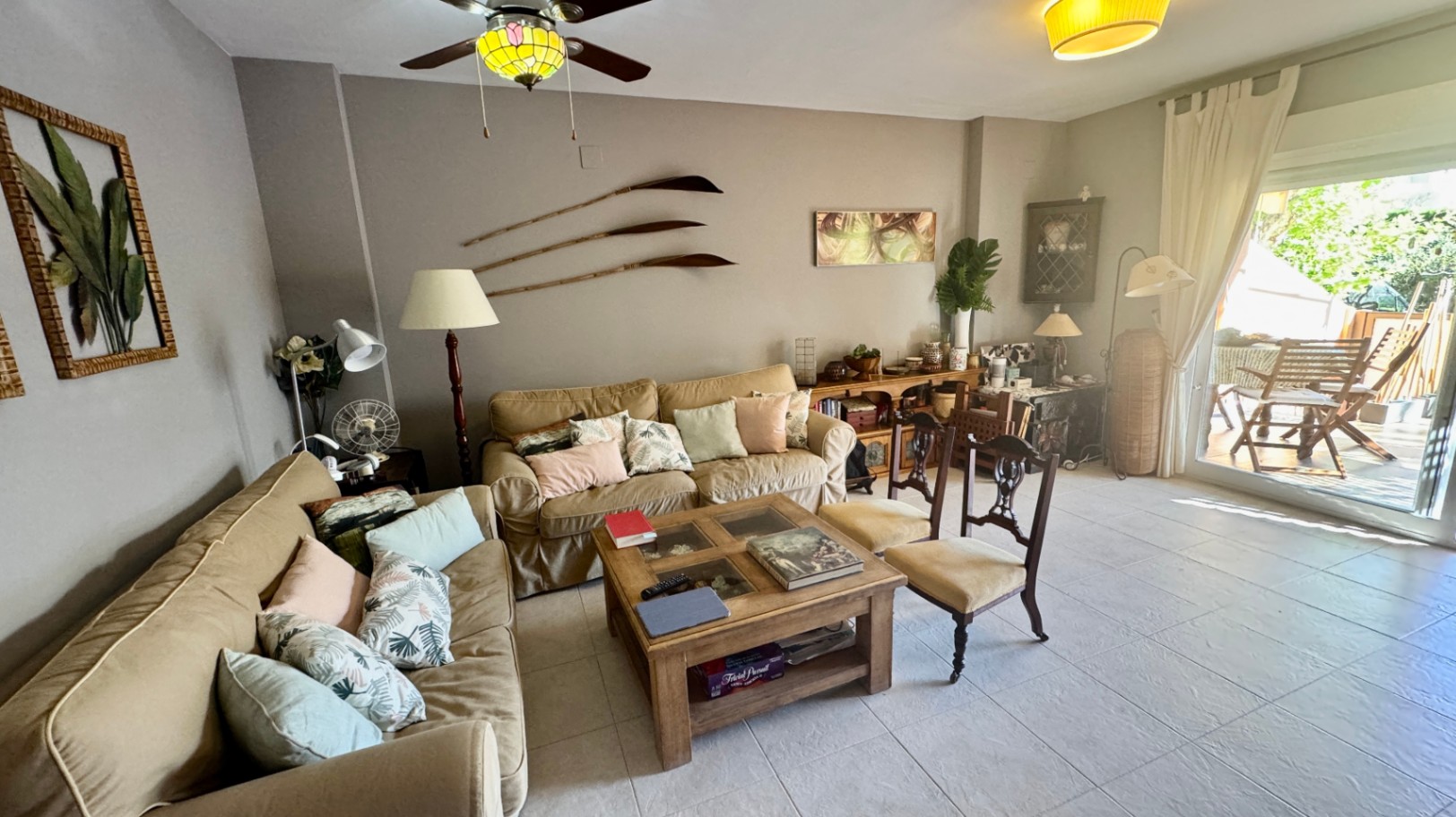 Salón amueblado con sofás en tonos tierra, mesa de centro de madera y acceso directo a una terraza exterior mediante puertas acristaladas.