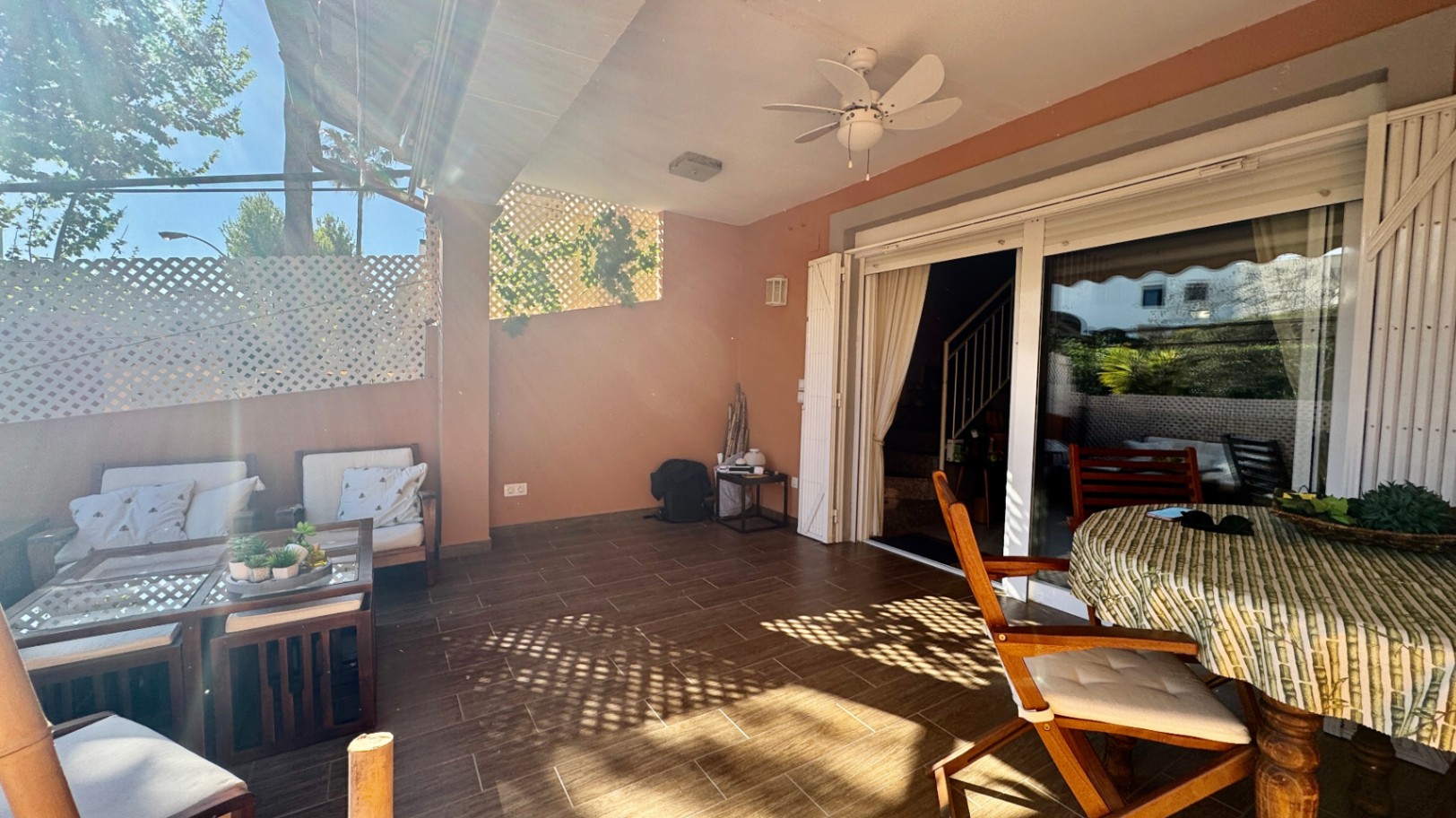 Terraza cubierta con suelo de gres, ventilador de techo y puertas correderas de cristal. Dispone de zona de estar y comedor exterior protegida por celosías.