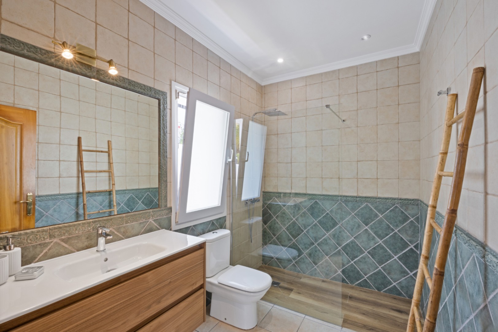 Baño con ducha a ras de suelo, suelo de efecto madera, azulejos verdes en forma de diamante, mueble de lavabo de madera y escalera decorativa de bambú.