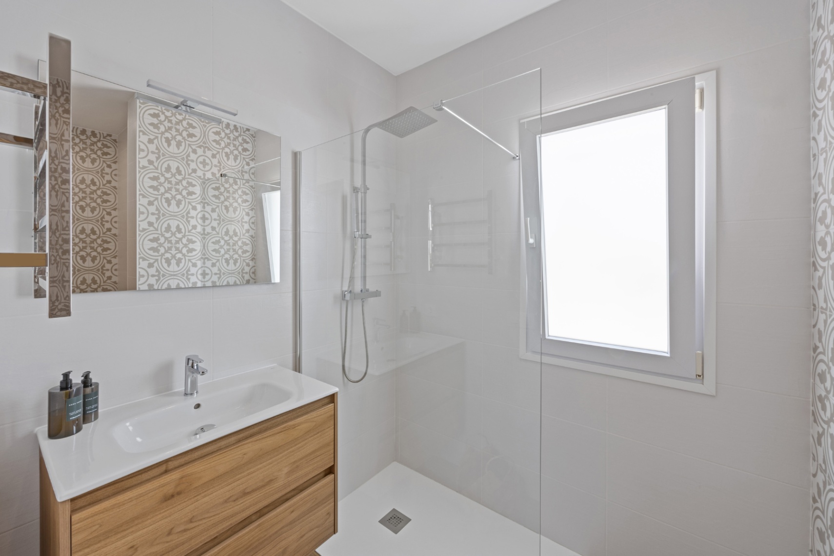 Baño contemporáneo con mueble de madera, lavabo cerámico y ducha de obra con mampara de cristal, complementado por azulejos con detalles hidráulicos.