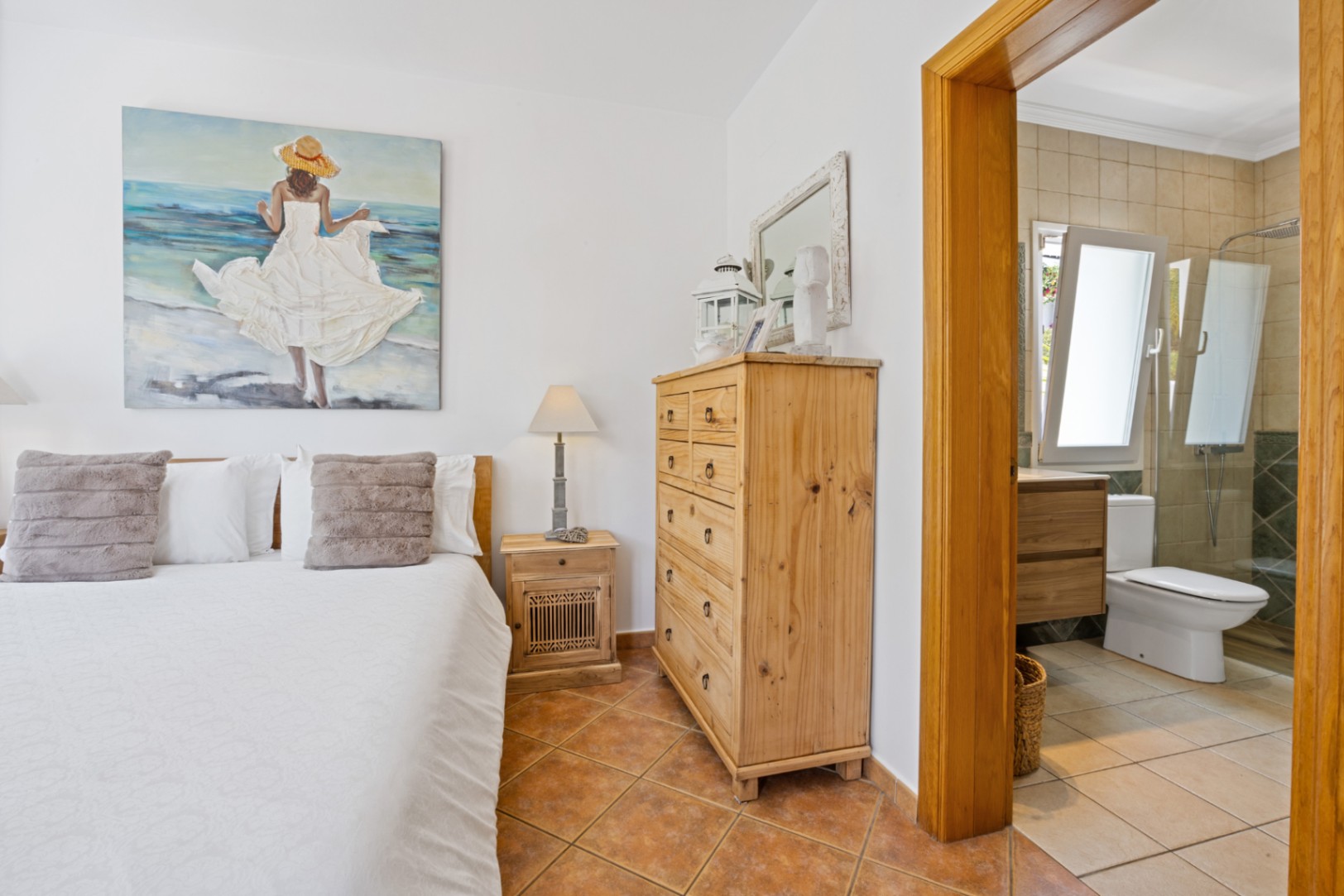 Dormitorio con suelos de terracota y mobiliario de madera rústica, que incluye un baño en suite con ducha de obra y mampara de cristal.