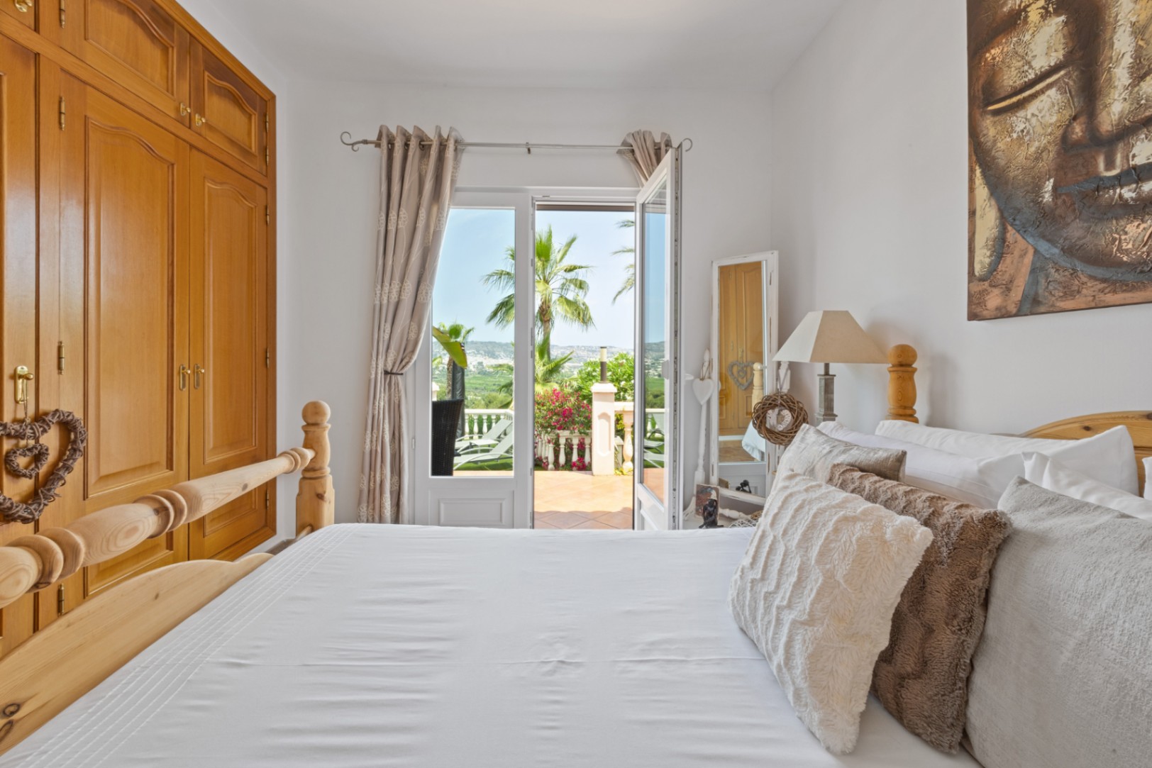 Dormitorio luminoso con armario empotrado de madera y cama a juego, con acceso directo a una terraza con vistas despejadas y palmeras.