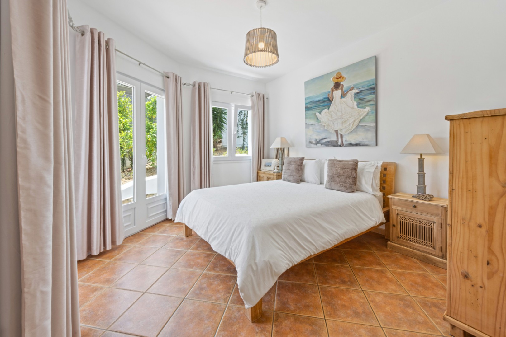 Dormitorio luminoso con suelos de baldosas de terracota, mobiliario de madera y puertas acristaladas con acceso directo al jardín y luz natural.