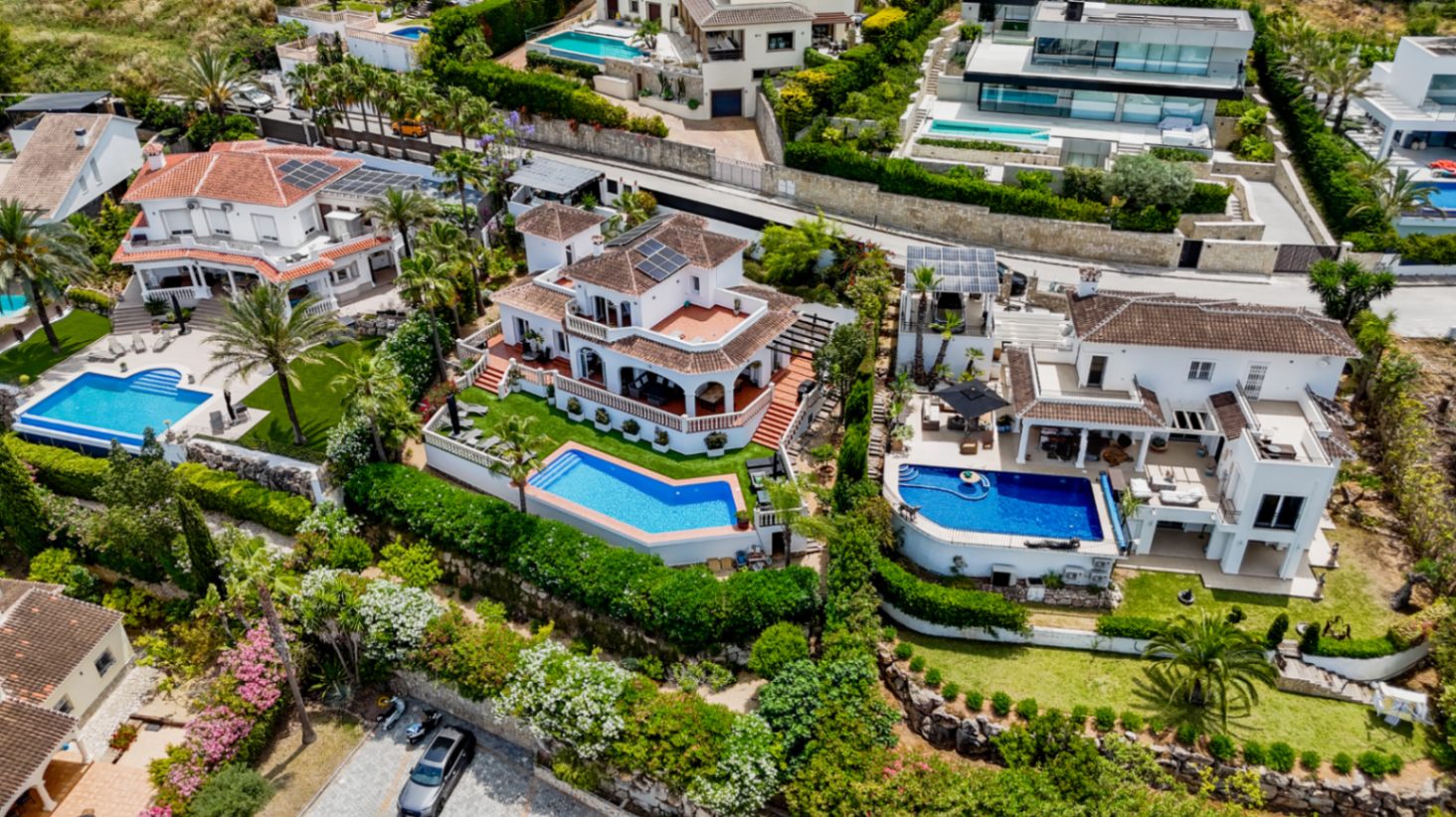 Perspectiva aérea de villas mediterráneas de lujo con piscinas privadas, tejados de terracota, paneles solares y jardines integrados en la ladera.