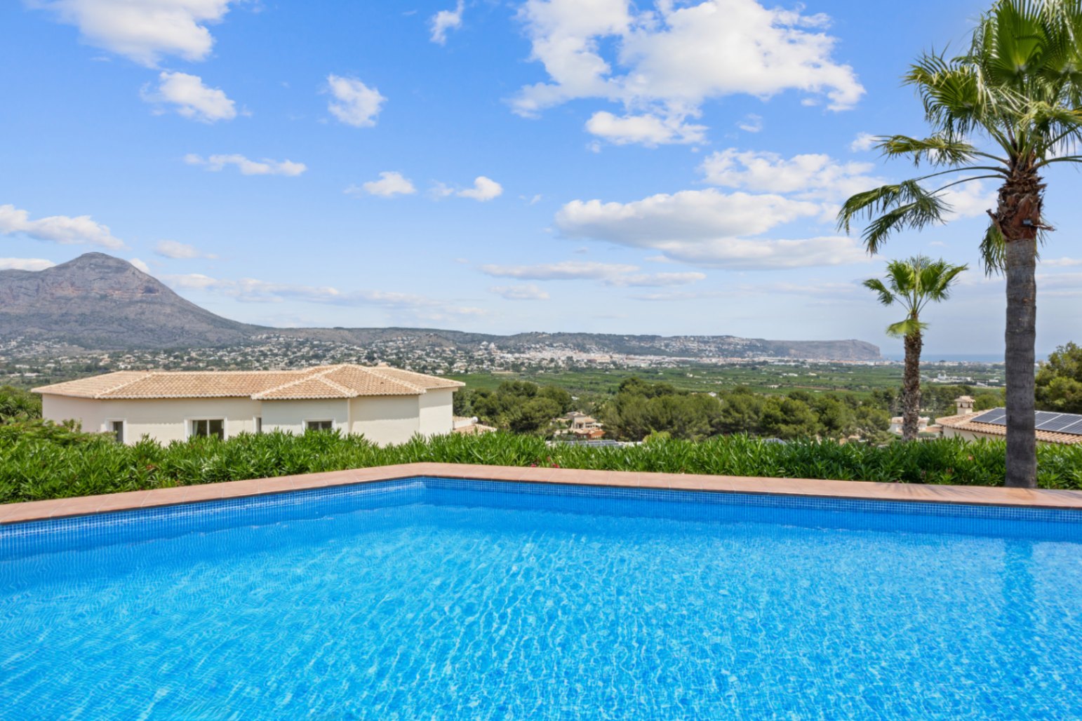 Piscina con gresite azul y borde de terracota, con vistas panorámicas al valle y a las montañas bajo un cielo despejado.