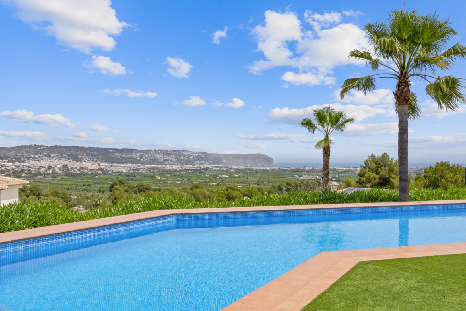 Piscina de forma curva con gresite azul y borde de terracota, destacando las vistas panorámicas al valle y las montañas circundantes.