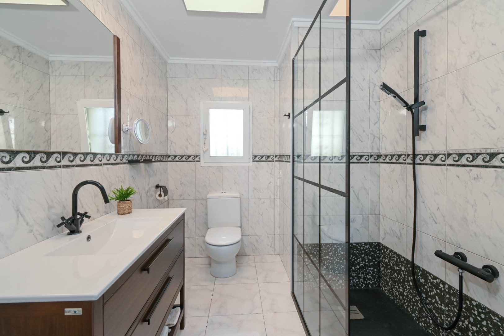 Baño moderno con azulejos efecto mármol, mueble de madera oscura con grifería negra y ducha con mampara de estilo industrial y plato oscuro.