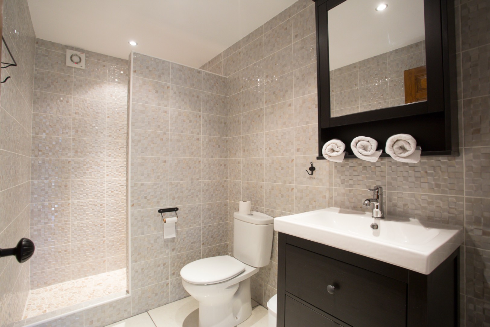 Baño moderno con ducha a ras de suelo revestida de mosaico, mueble de lavabo en madera oscura y armario con espejo coordinado.